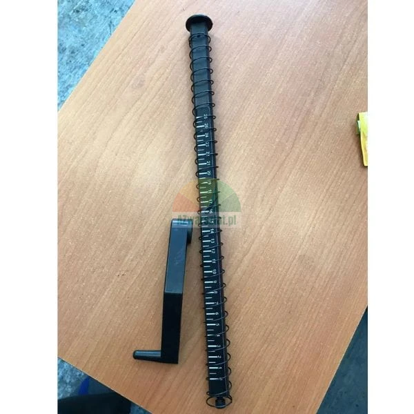 Long black binding machine element with a scale and a plastic crank on a table.