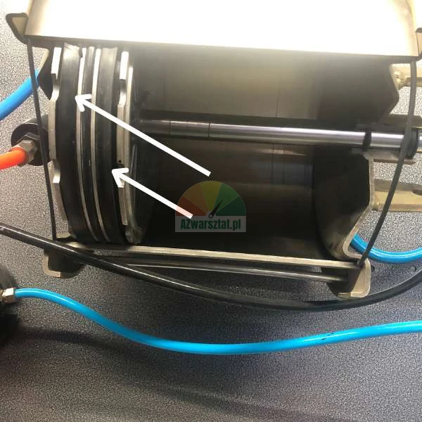 Interior of an industrial device showing a piston and seals indicated by white arrows.