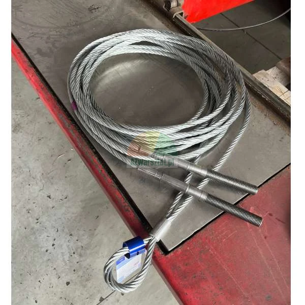 Coiled steel wire rope with threaded ends and an eye loop on a metal workbench.