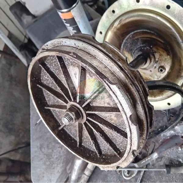 Metal mechanical part with spokes and a central nut in a workshop setting.